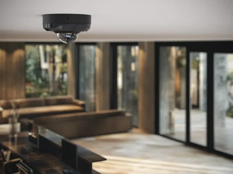 Caméra dôme Ajax DomeCam Mini noire fixée au plafond d'une pièce de vie avec grandes baies vitrées
