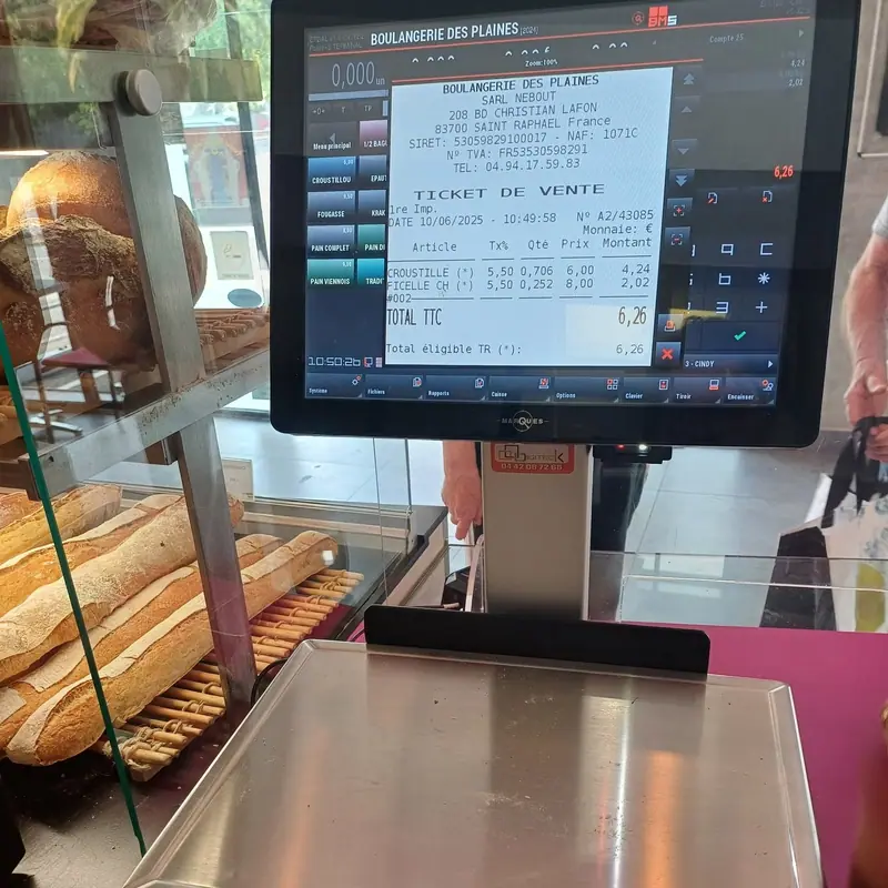 Écran de caisse affichant un ticket de vente devant la vitrine à baguettes d'une boulangerie