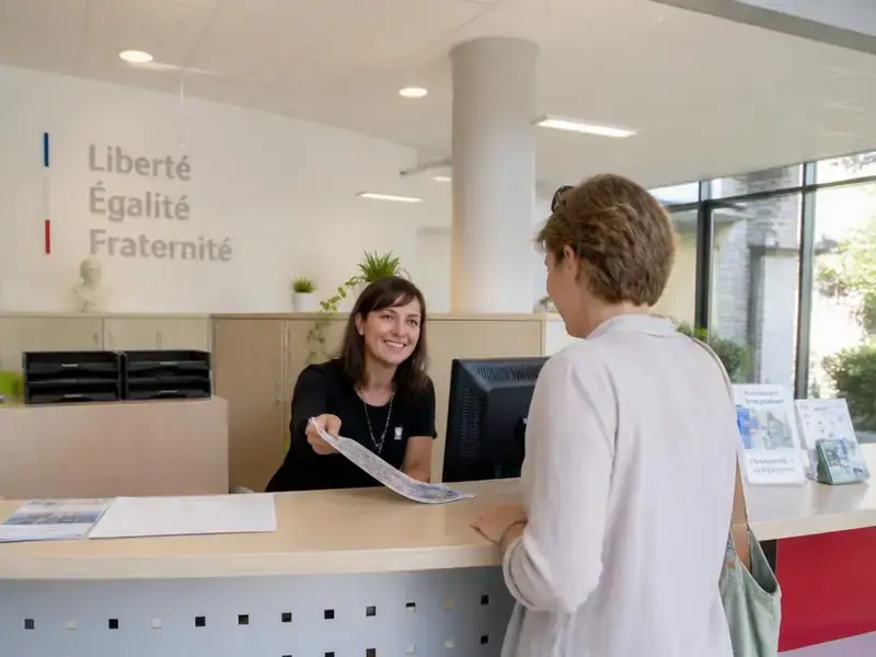 Agent d'accueil d'un office de tourisme qui renseigne des visiteurs devant son comptoir