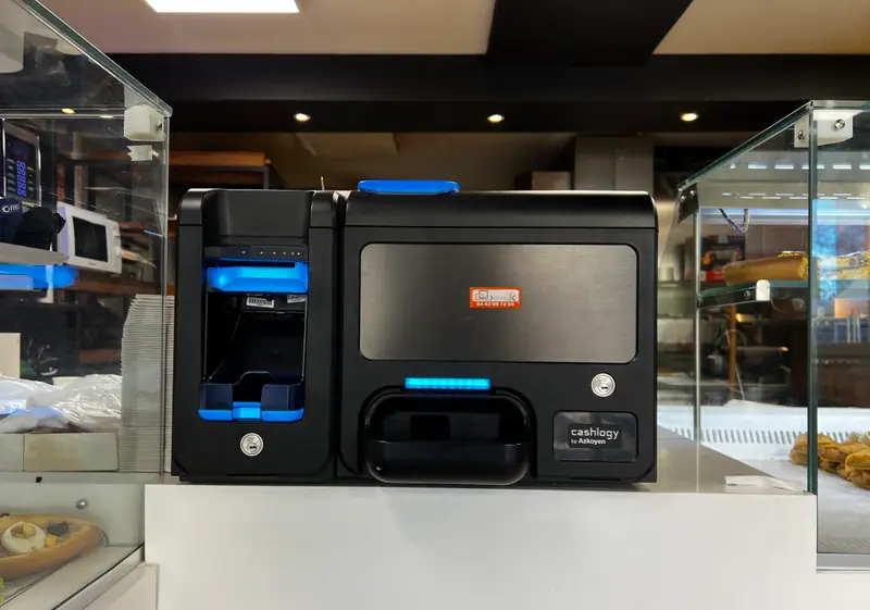 Monnayeur Cashlogy avec étiquette ECR Digiteck posé sur un comptoir entre deux vitrines réfrigérées