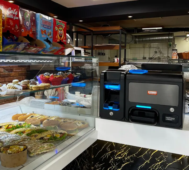 Monnayeur automatique Cashlogy installé par ECR Digiteck sur le comptoir d'un snack, devant la vitrine de sandwiches