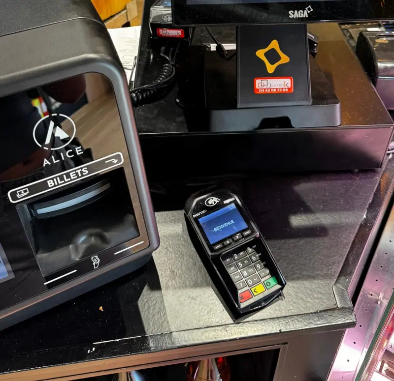 Terminal de paiement affichant « Bienvenue » devant un monnayeur automatique et une caisse équipés d'une étiquette ECR Digiteck